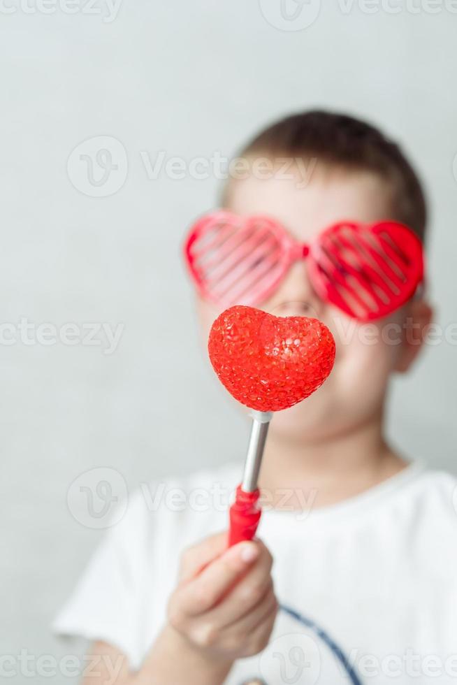 porträtt av en leende pojke i hjärtformade glasögon i en vit t-shirt mot en vit bakgrund foto