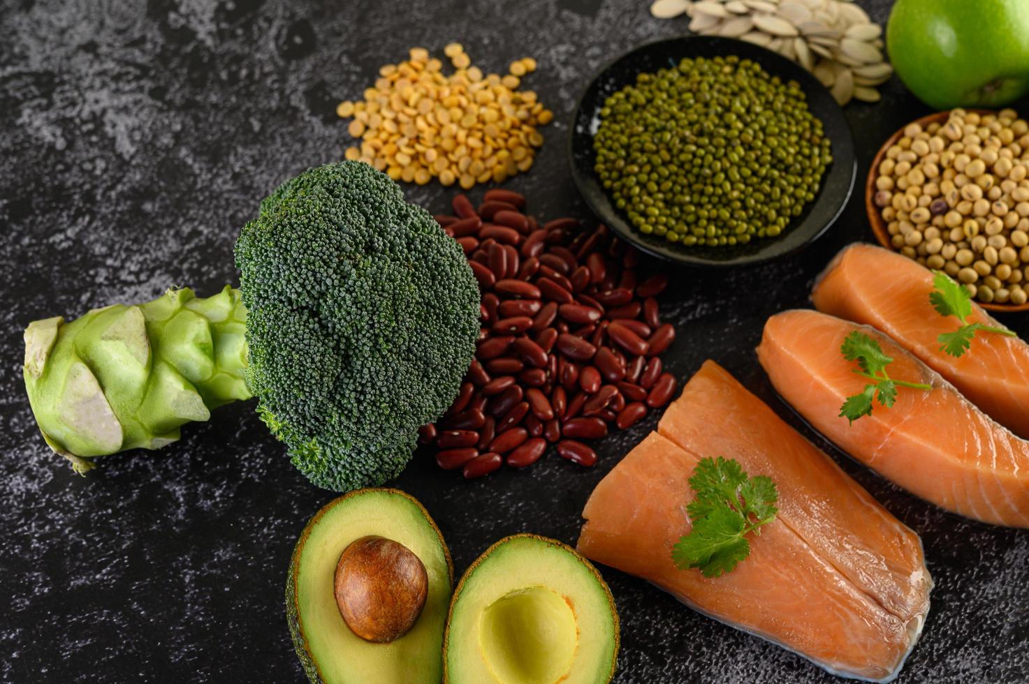 baljväxter, broccoli, frukt och lax på svart cementbakgrund foto