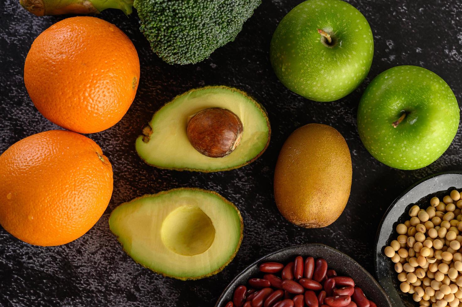 broccoli, äpple, apelsin, kiwi, avokado och bönor på en svart cementgolvbakgrund foto