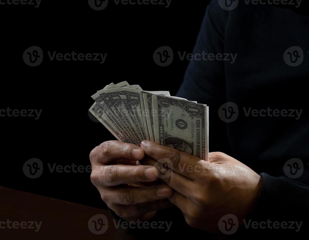 dator och händer av en man bär en svart skjorta, Sammanträde på en stol och en tabell, är en tjuv, innehav pengar, räkning de belopp erhållna från kapning eller råna, i en kolsvart rum. foto