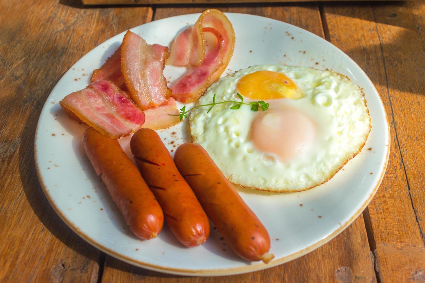 bacon, stekte ägg och korv på den vita plattan och träbord foto