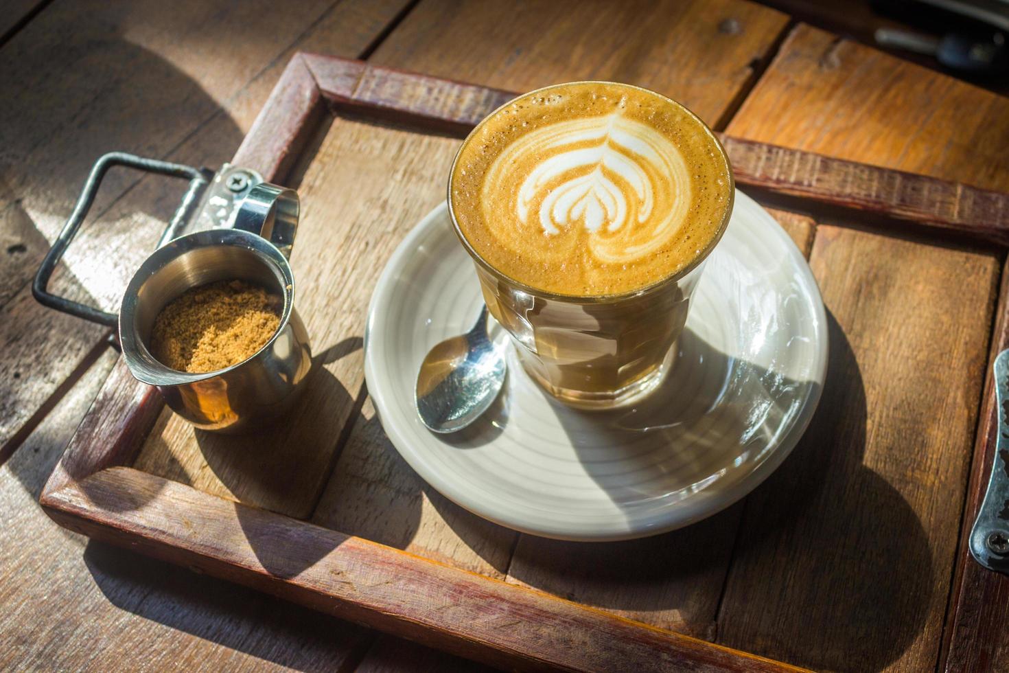 kaffe med lattekonst på träbricka i solljus foto