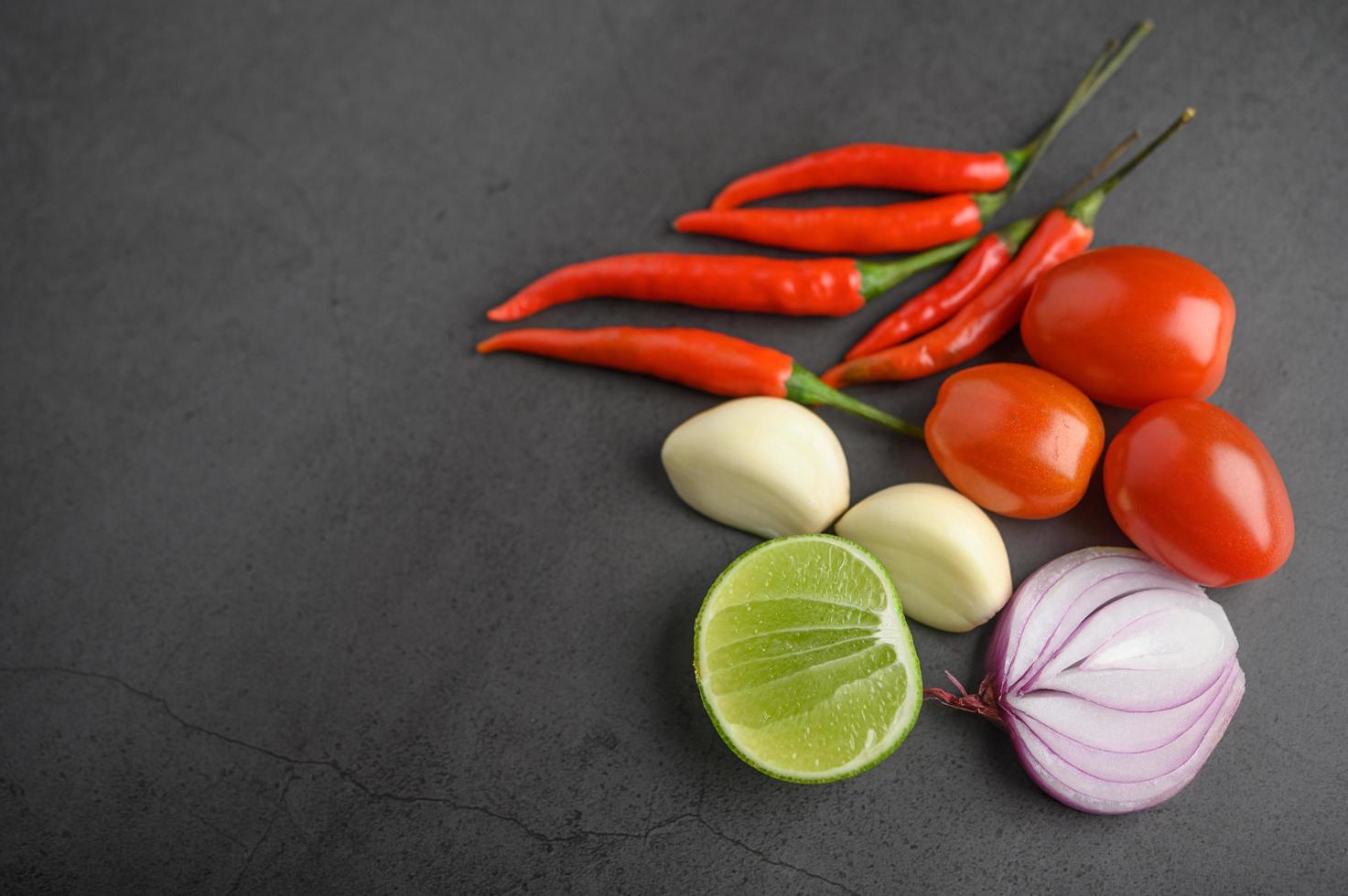 limeskivor, schalottenlök, vitlök, tomater och paprika på ett svart cementgolv foto