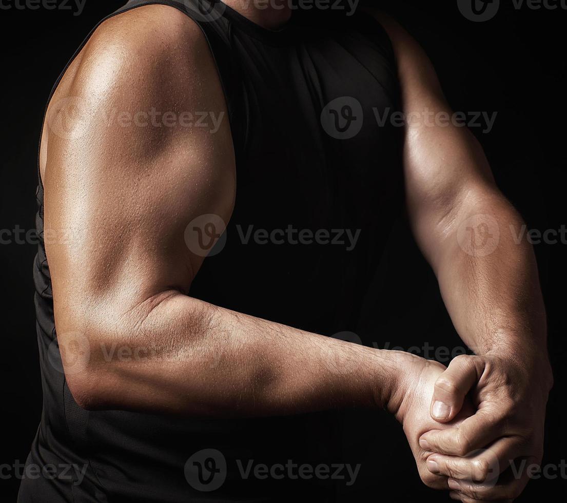 vuxen man med en sporter figur i svart kläder spänd hans muskler i hans vapen foto