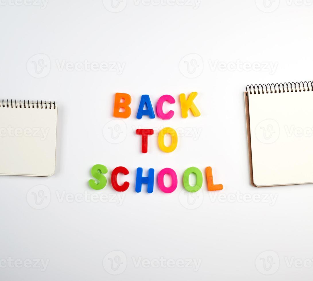 inskrift tillbaka till skola från flerfärgad plast brev och en stack av bärbara datorer med tom vit ark foto