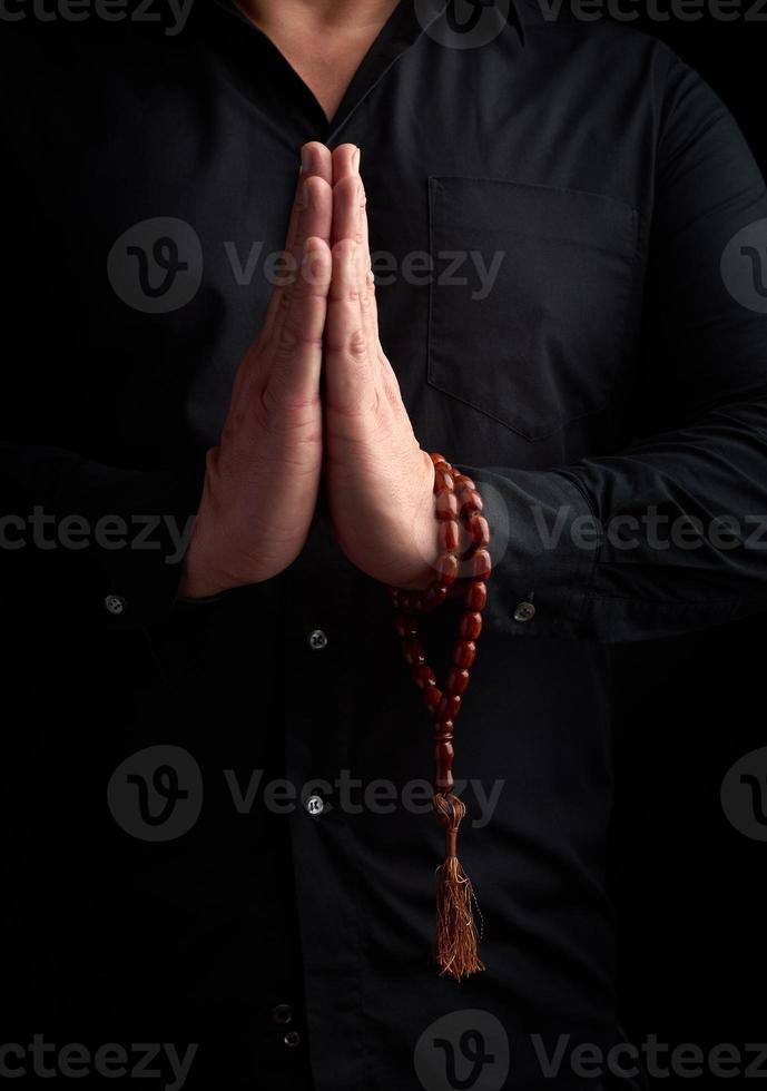 vuxen man i en svart skjorta vikta hans vapen i främre av hans bröst i en bön utgör foto