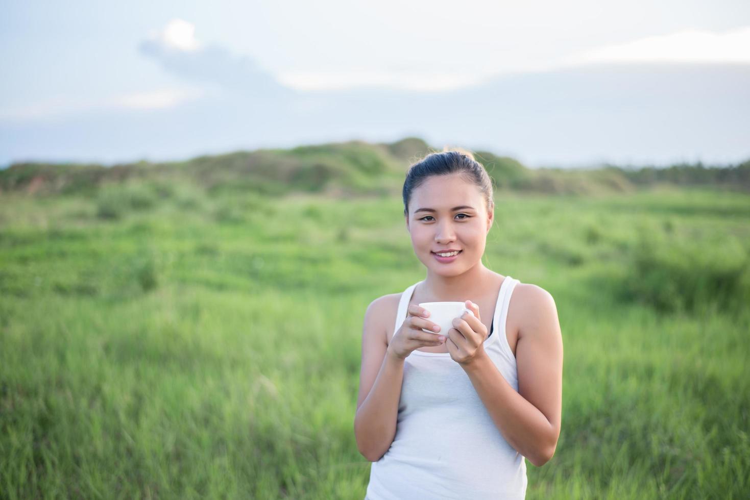 vacker asiatisk kvinna som dricker kaffe på en äng foto