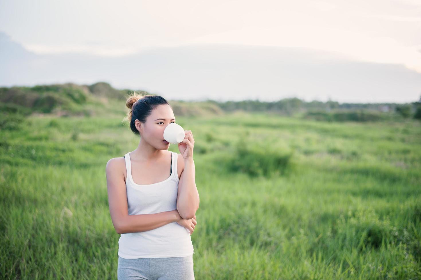 vacker asiatisk kvinna som dricker kaffe på en äng foto