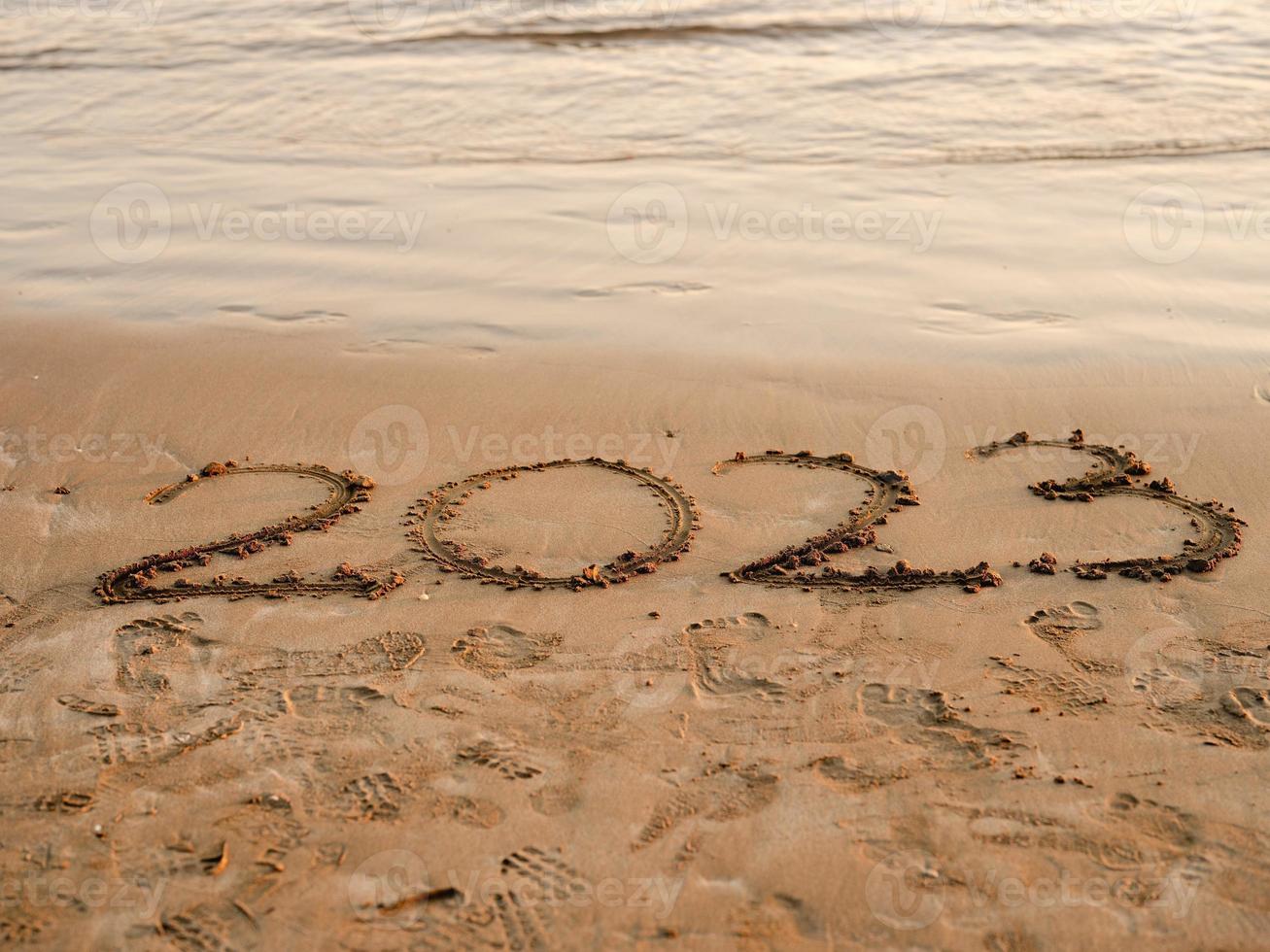 ny år begrepp Foto. tal 2023 handskriven i de sand yta. mjuk hav Vinka och strand på bakgrund. foto