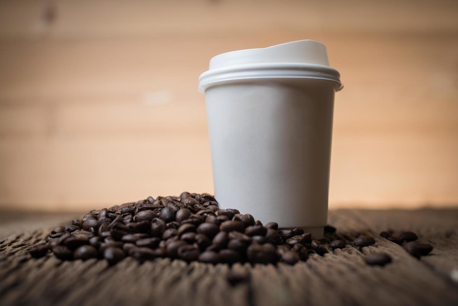 pappers kaffekopp med kaffebönor på ett träbord foto