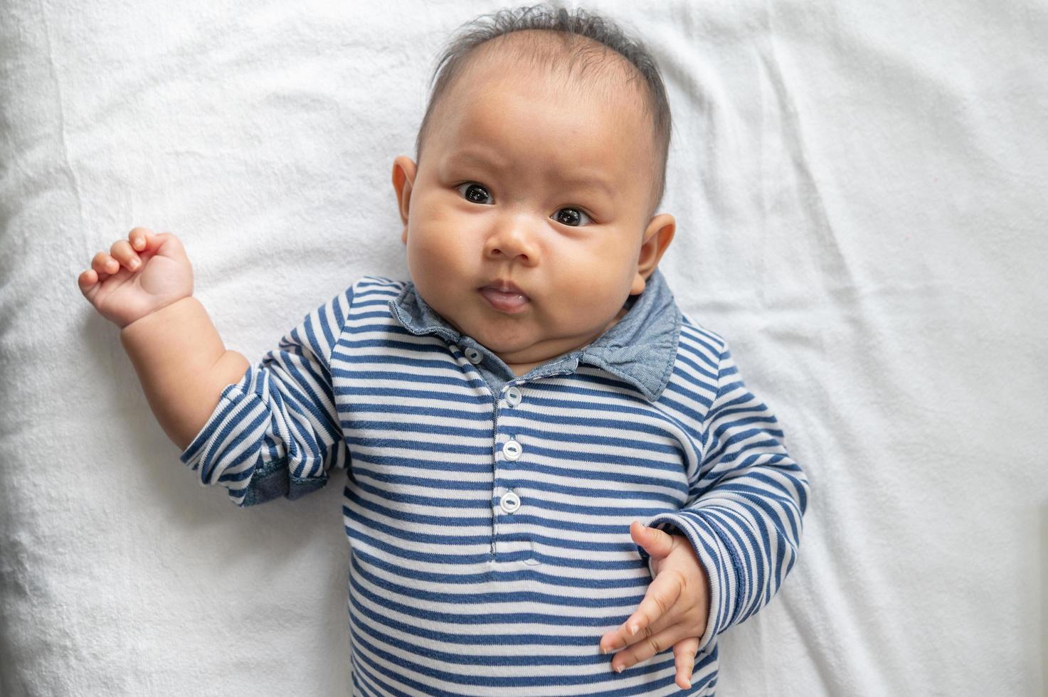 baby som ligger med ansiktet uppåt på en vit säng och tittar på kameran foto