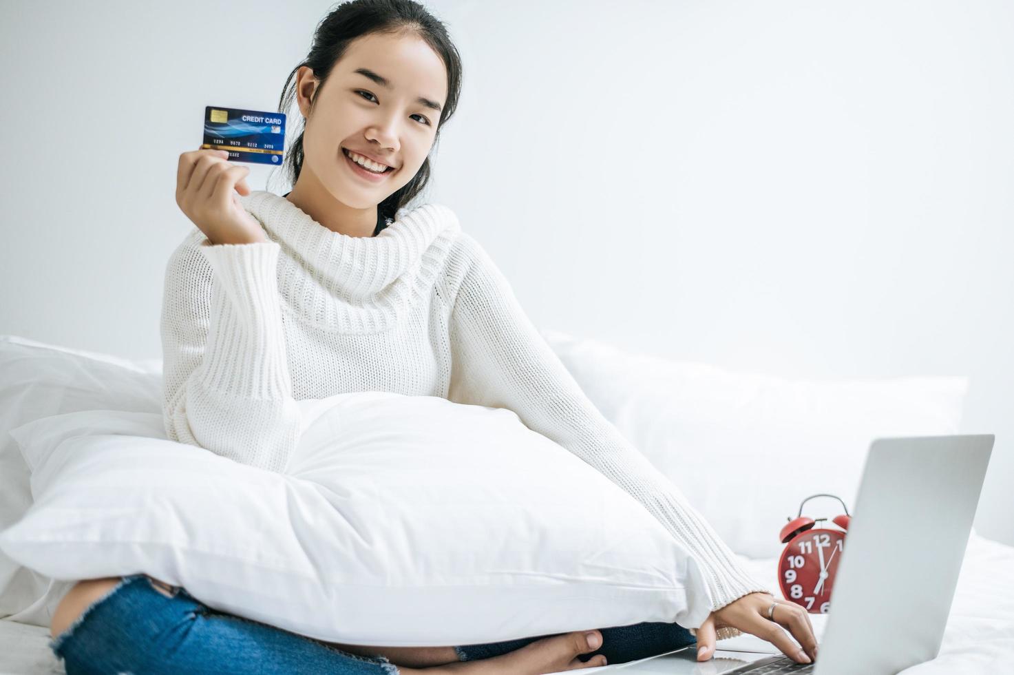 ung kvinna som shoppar på bärbara datorn och innehar ett kreditkort foto