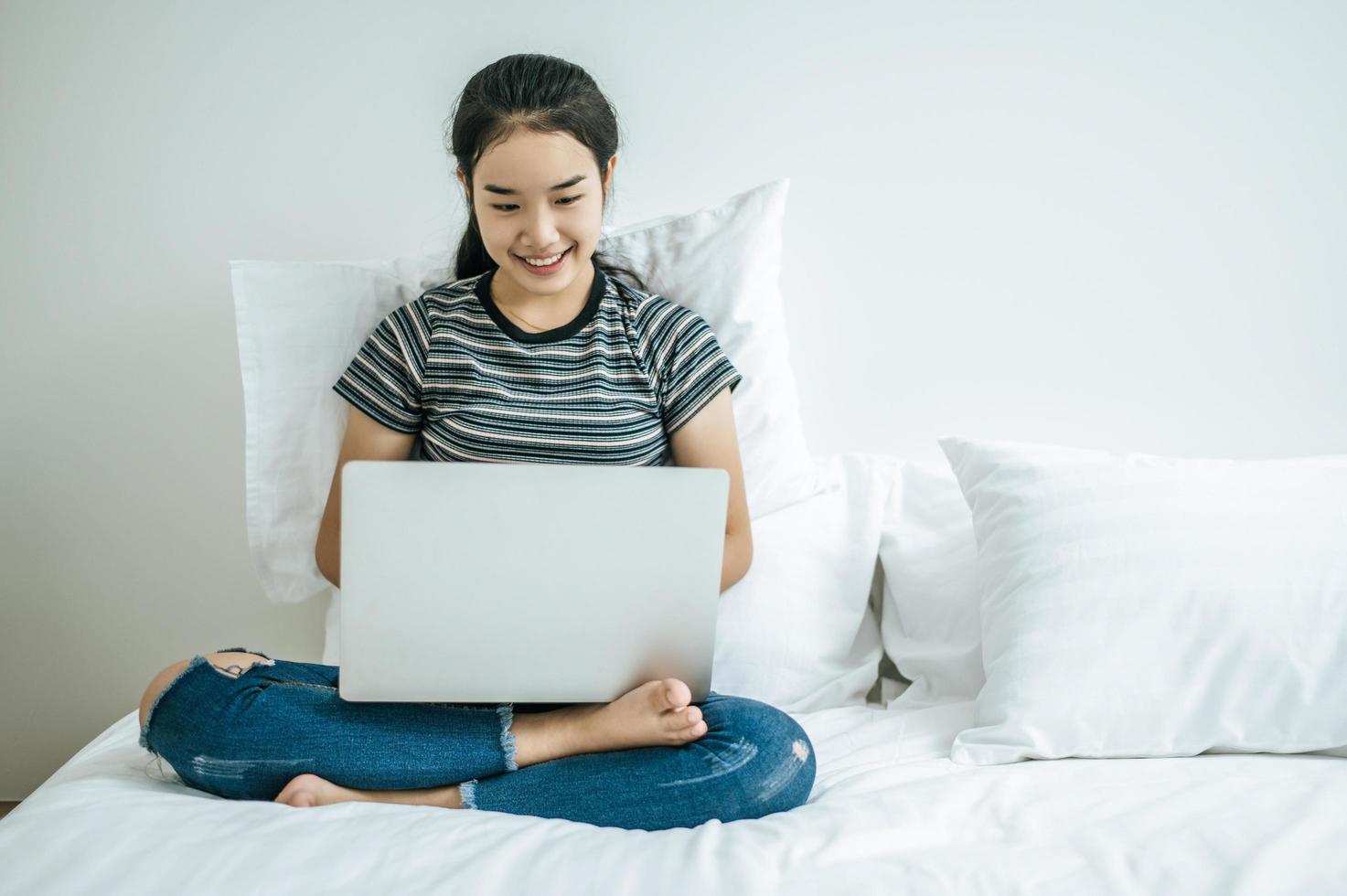 en ung kvinna som leker på sin bärbara dator i sängen foto