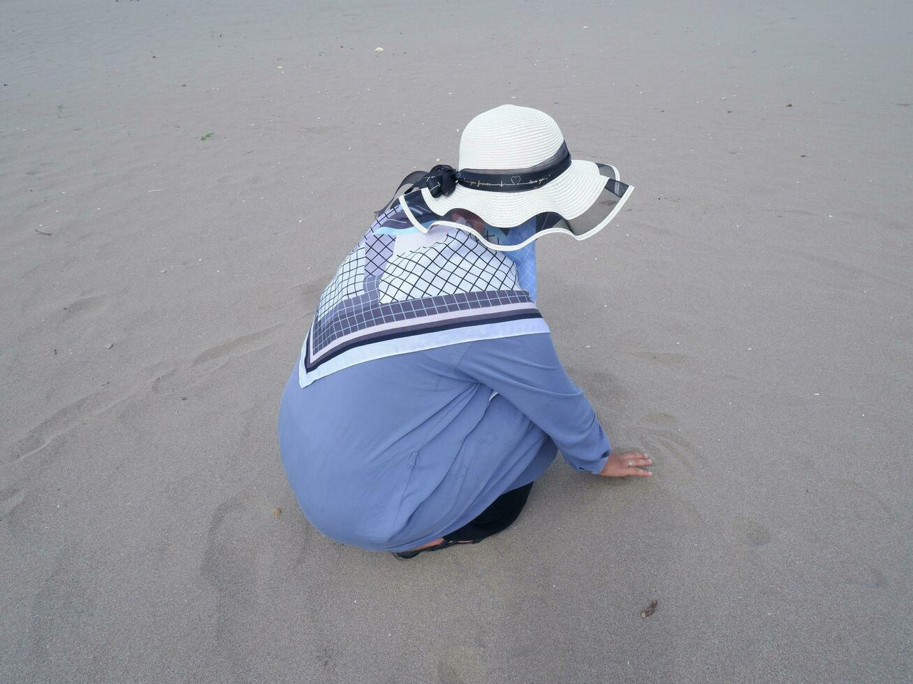 tillbaka av de kvinna i de hatt vem var Sammanträde och spelar strand sand, de se av de sand foto