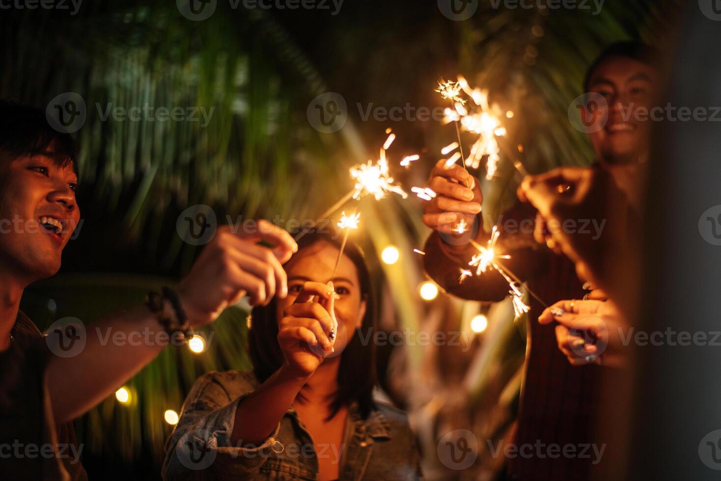 porträtt av Lycklig asiatisk grupp av vänner har roligt med sparklers utomhus- - ung människor har roligt med fyrverkeri på natt tid - människor, mat, dryck livsstil, ny år firande begrepp. foto