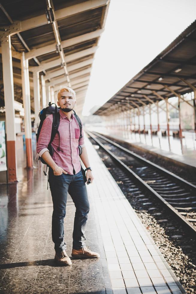 ung hipster man väntar på station plattform med ryggsäck foto