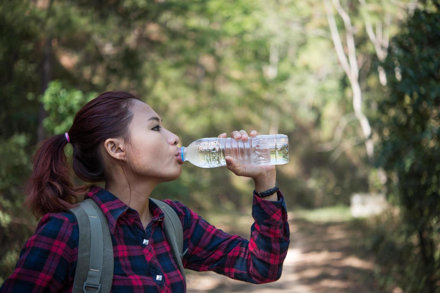 glad kvinna turist med ryggsäck dricksvatten i naturen foto