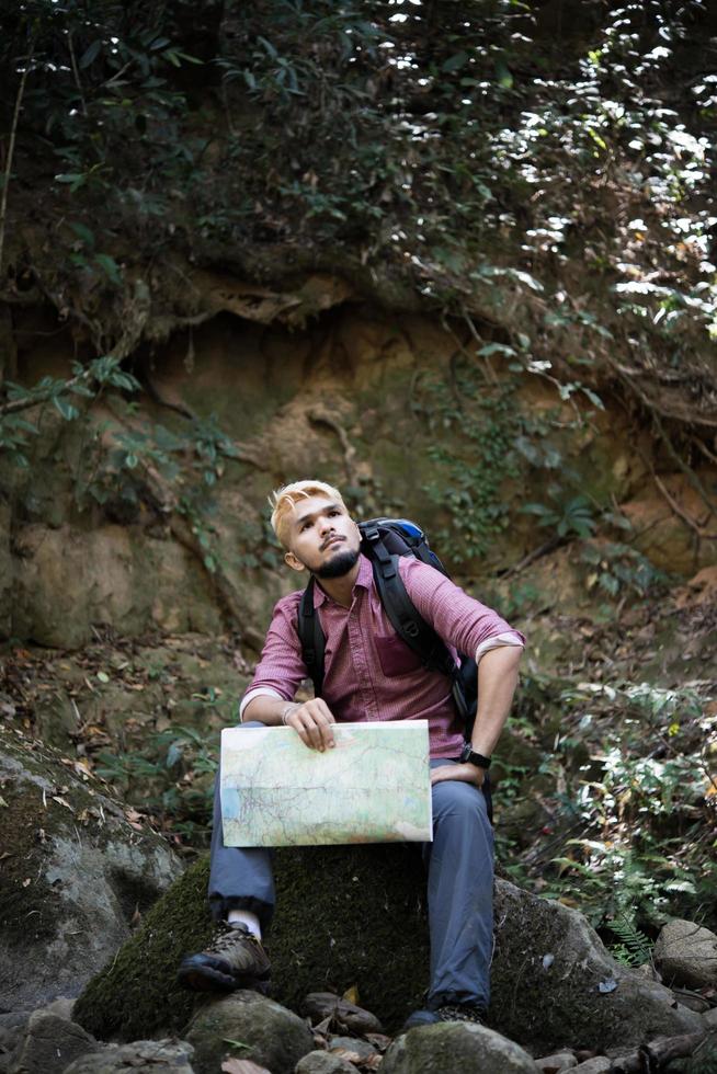 ung trött vandrare med ryggsäck sitter i skogen foto