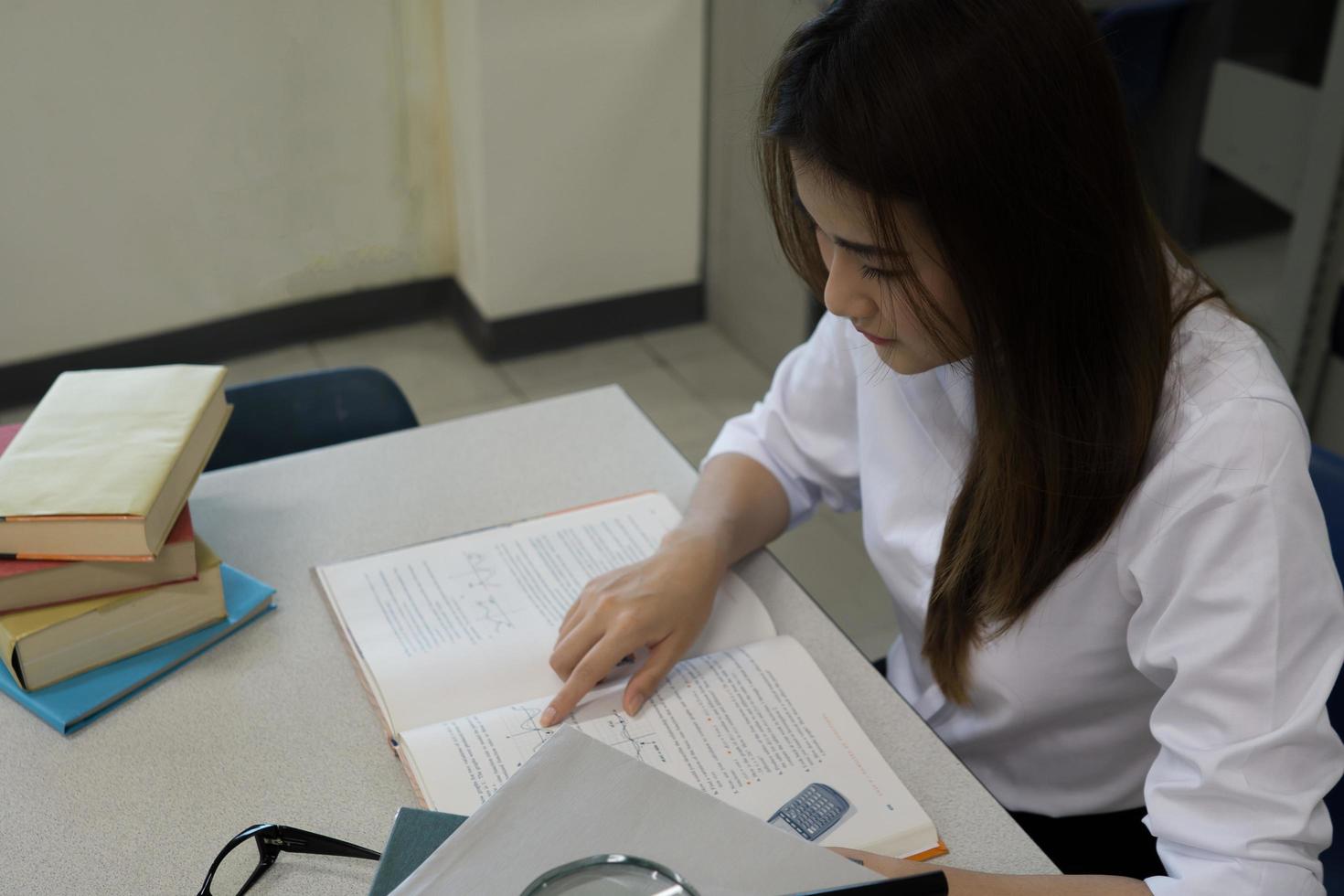 ung asiatisk student läser i biblioteket foto