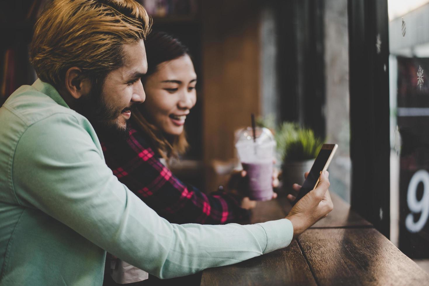 hipster par på semester sitter i inomhus kafé tittar på telefonen tillsammans foto