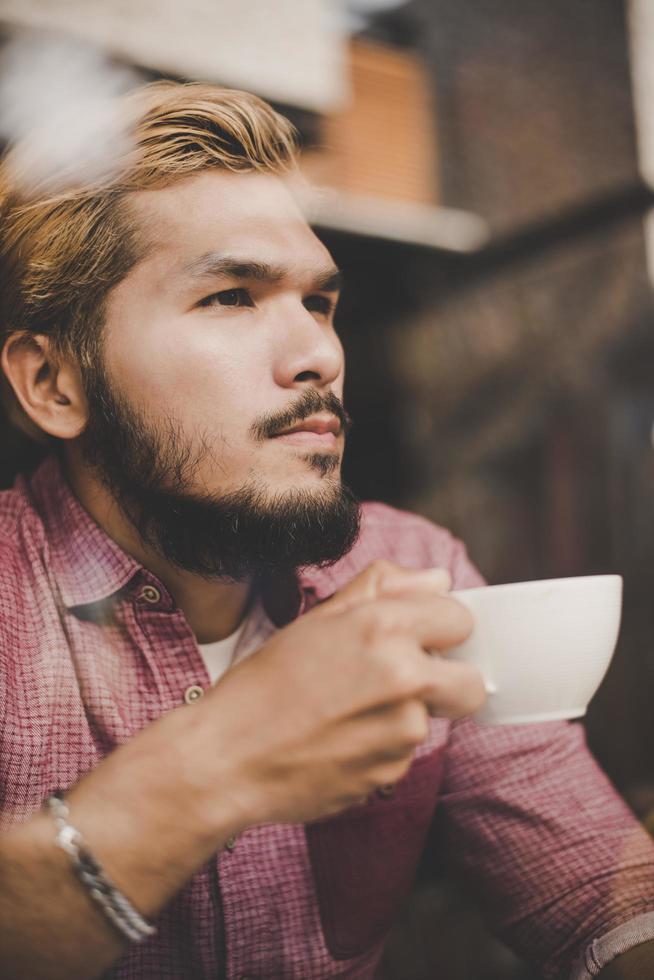 ung man sitter på ett kafé och dricker en kaffe foto