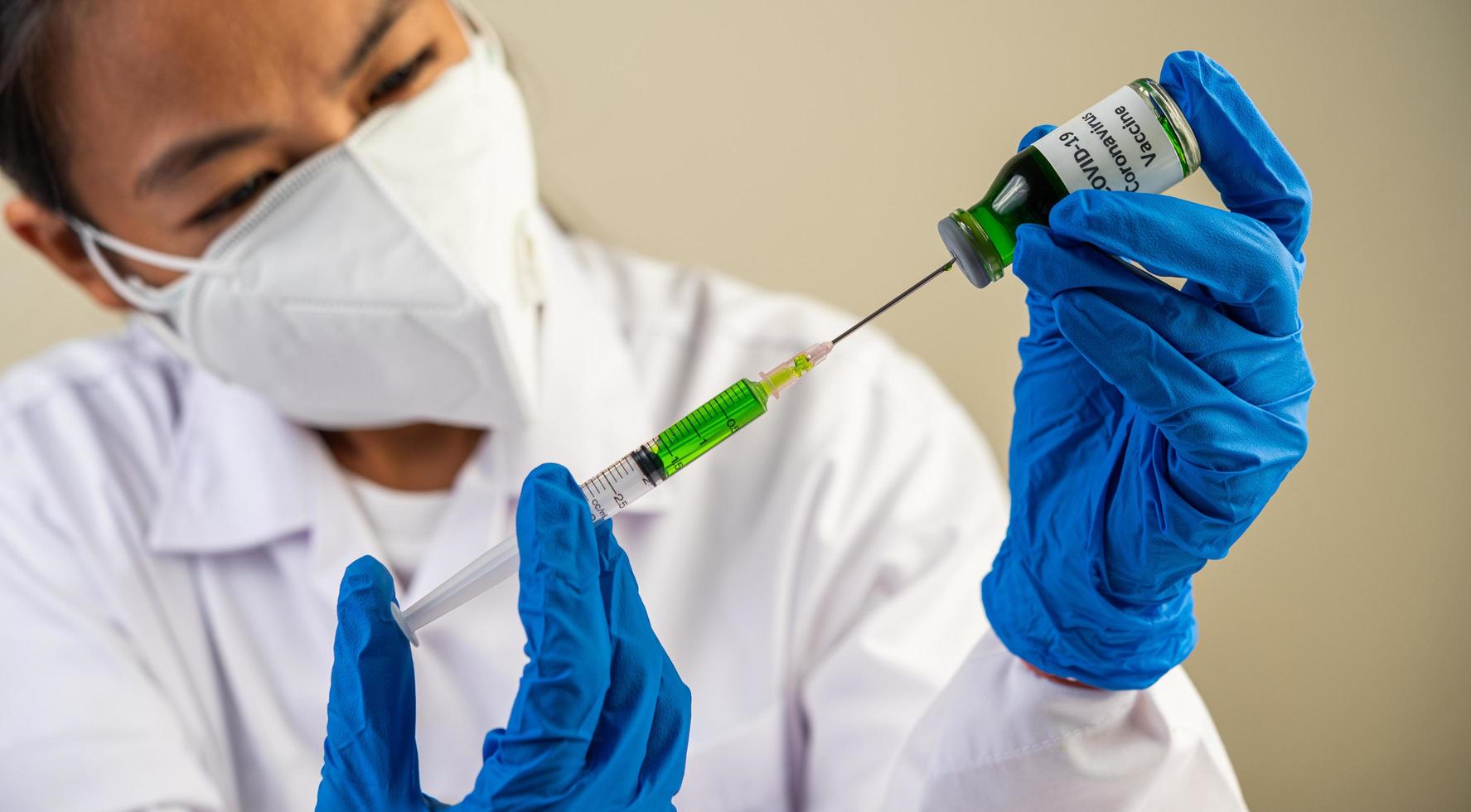 forskare som bär skyddsmasker och handskar som håller en spruta med ett vaccin för att förhindra covid-19 foto