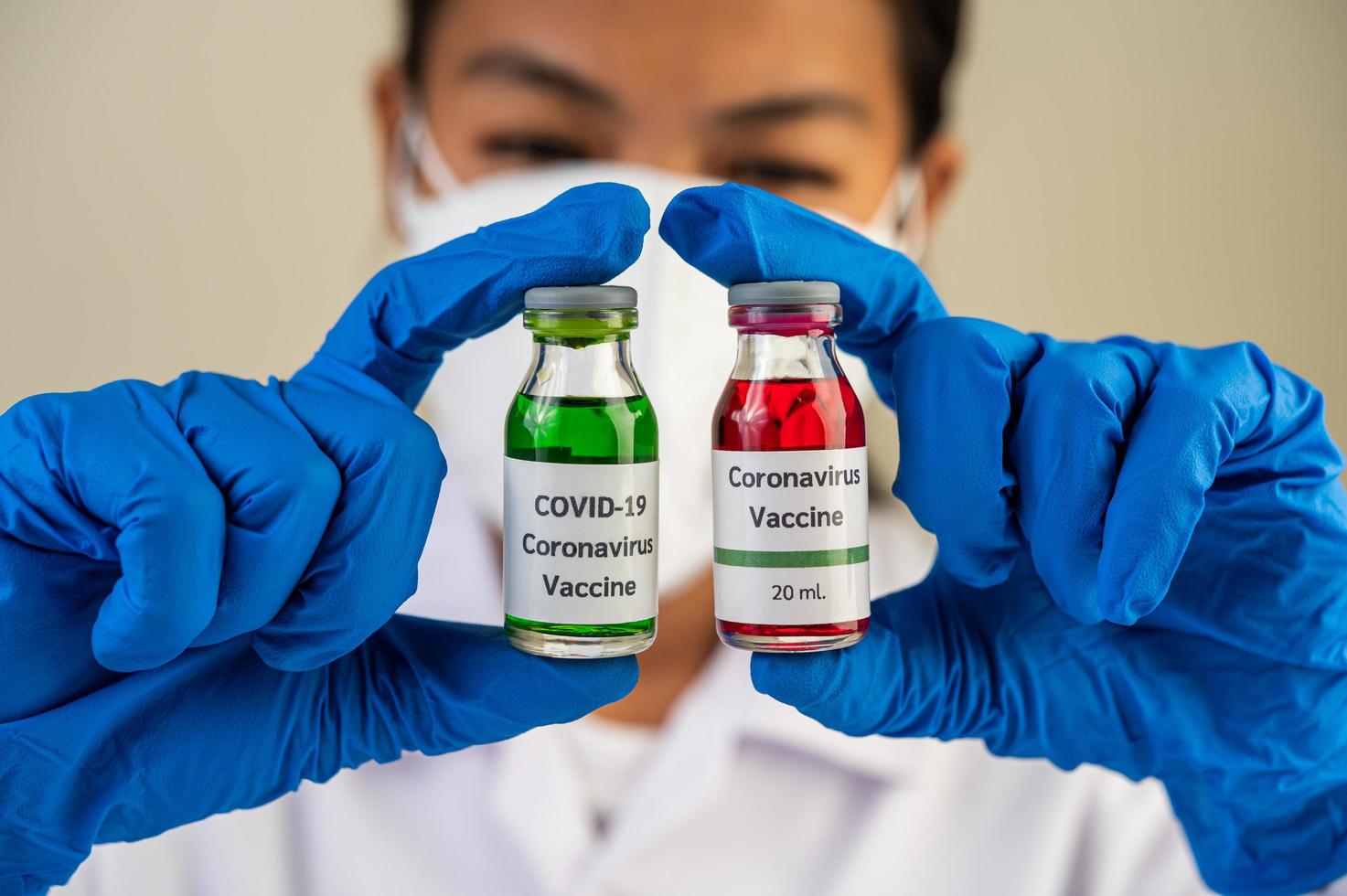 en forskare som bär mask och handskar bär flaskor med vacciner för att skydda mot covid-19 foto
