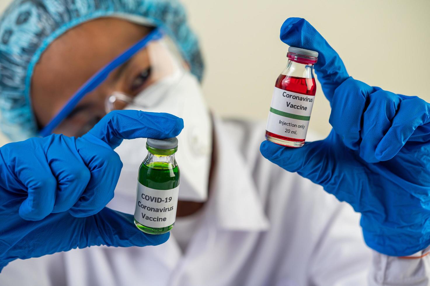 en forskare som bär mask och handskar bär flaskor med vacciner för att skydda mot covid-19 foto
