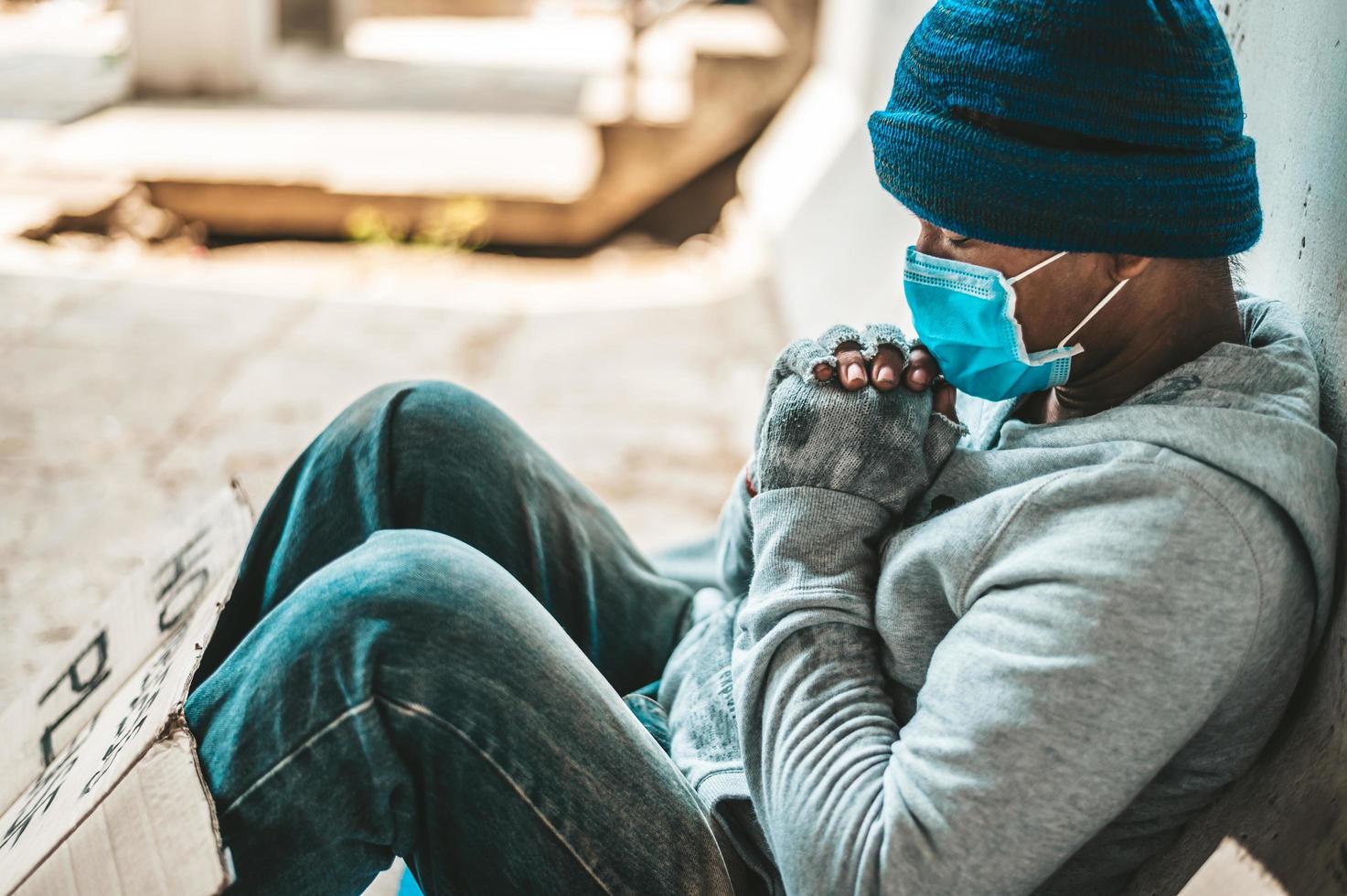 mannen sitter bredvid gatan och bär en medicinsk mask med ett hemlöst meddelande foto