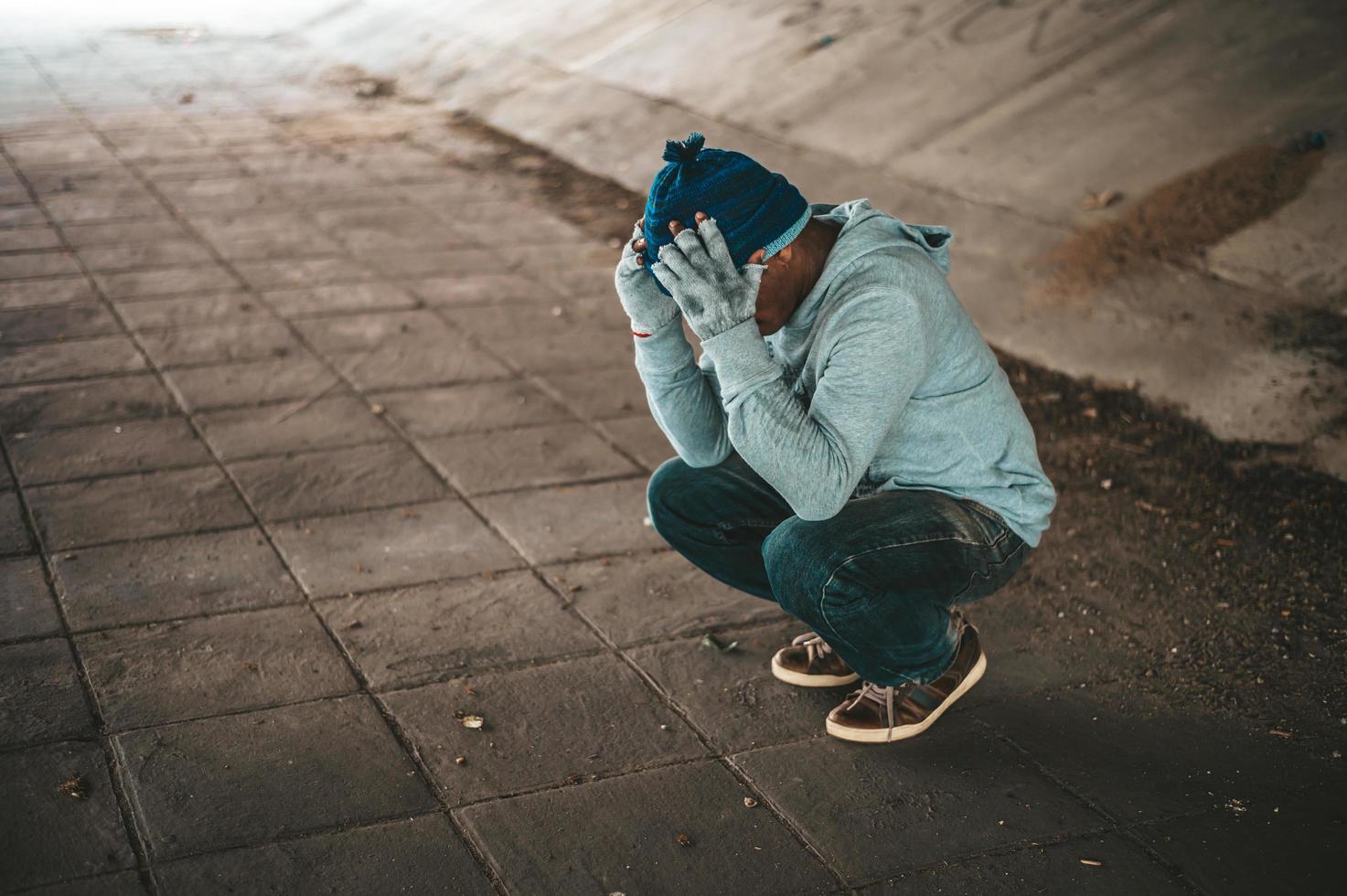 hemlös man sitter under bron med båda händerna som håller huvudet foto