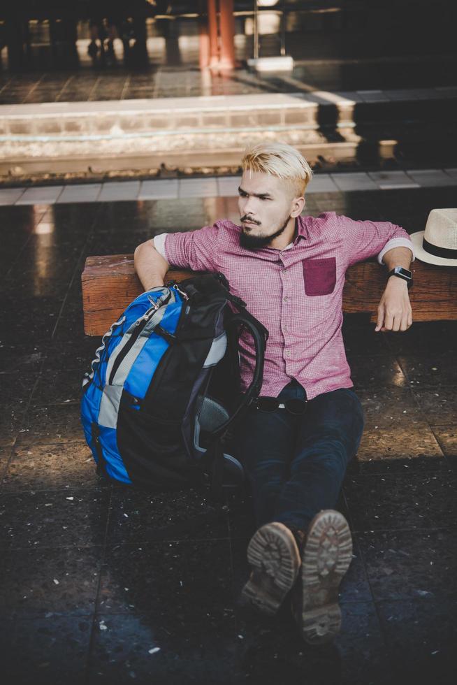 ung hipster man sitter på träbänk på järnvägsstationen foto