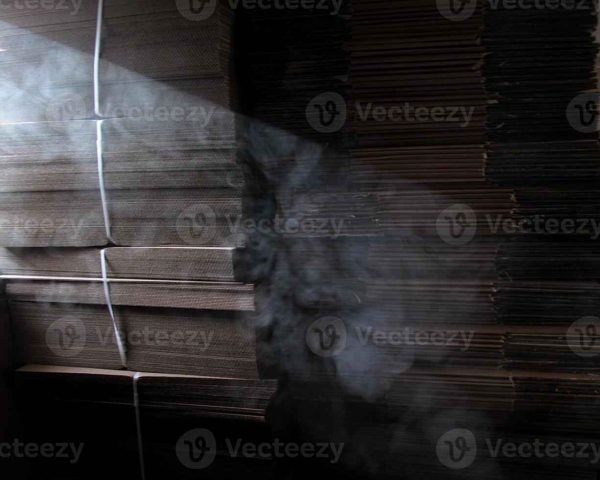 rök i en strimma av ljus mot de bakgrund av staplade kartong lådor i en lager foto
