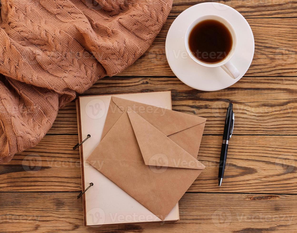 arbetsyta med anteckningsblock, kaffe kopp, kuvert och penna på en trä- tabell foto