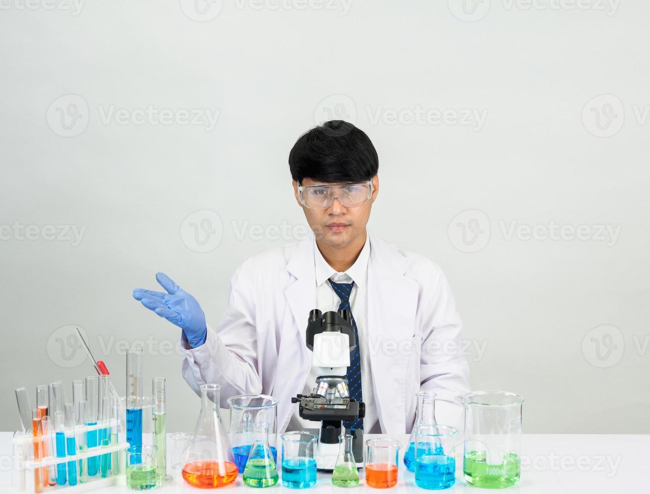 asiatisk manlig studerande forskare i reagens blandning laboratorium i en vetenskap forskning laboratorium med testa rör av olika storlekar och mikroskop. på de tabell i laboratorium kemi labb vit bakgrund. foto