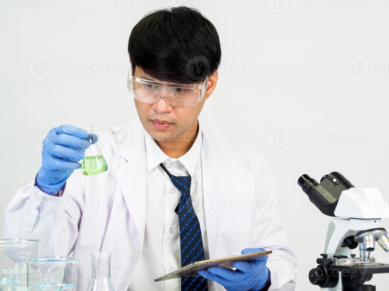 asiatisk manlig studerande forskare i reagens blandning laboratorium i en vetenskap forskning laboratorium med testa rör av olika storlekar och mikroskop. på de tabell i laboratorium kemi labb vit bakgrund. foto