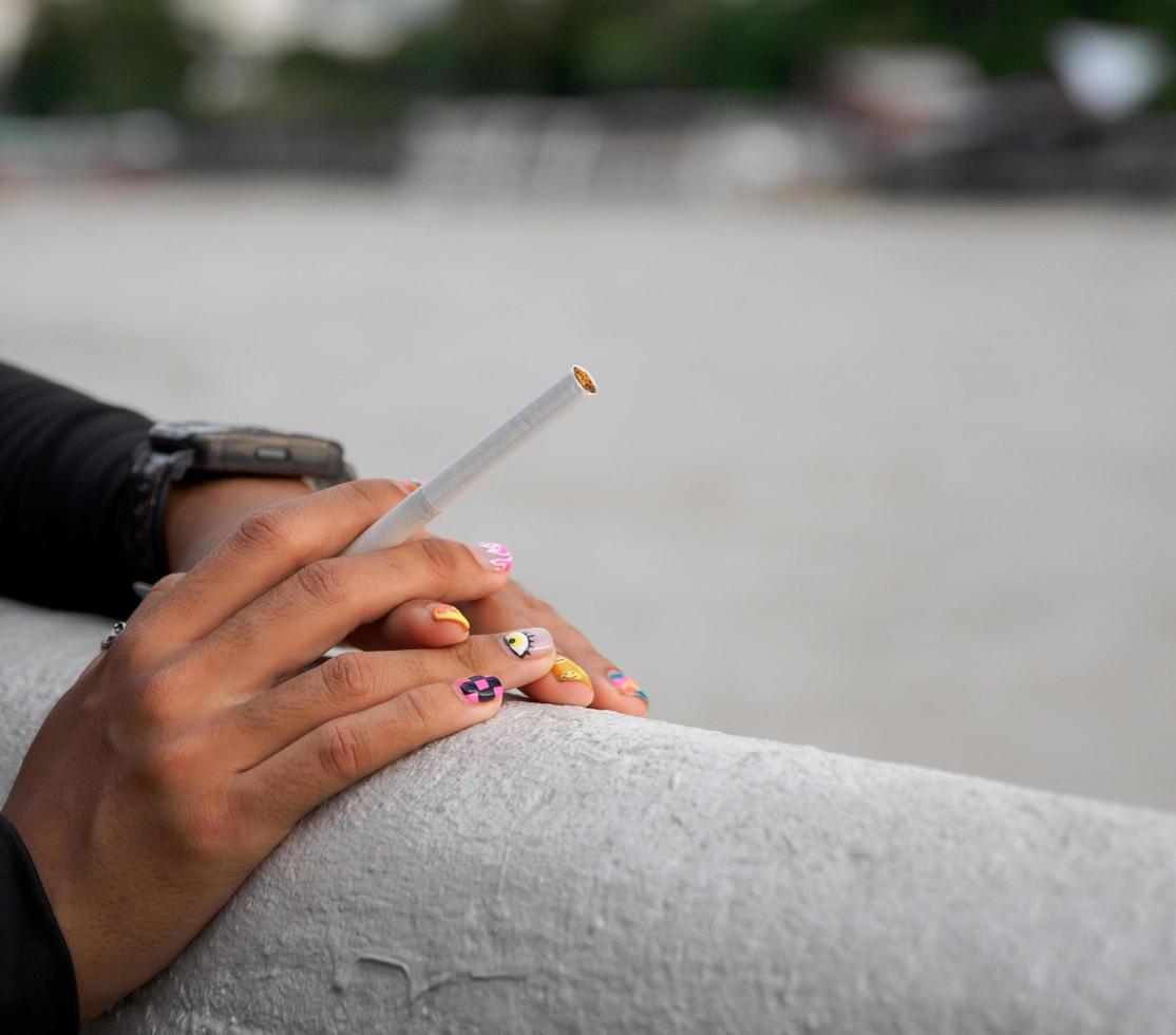 närbild hand kvinna tonåring ung Asien ett person bär en svart skjorta håll rökning cigarett vit Färg stående utomhus- förbi de vägg foto