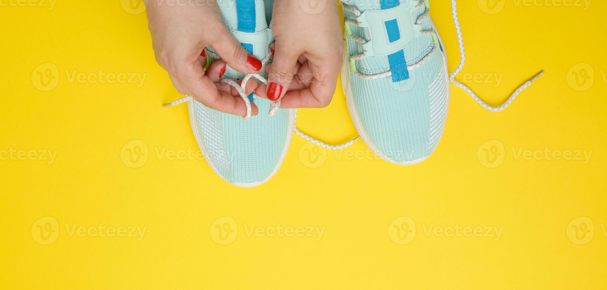två kvinna händer kvitt skosnören på blå textil- sneakers, topp se foto