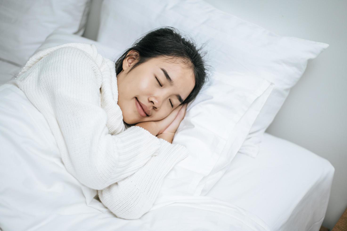 ung kvinna som bär vit skjorta som bara vaknar upp i sängen foto