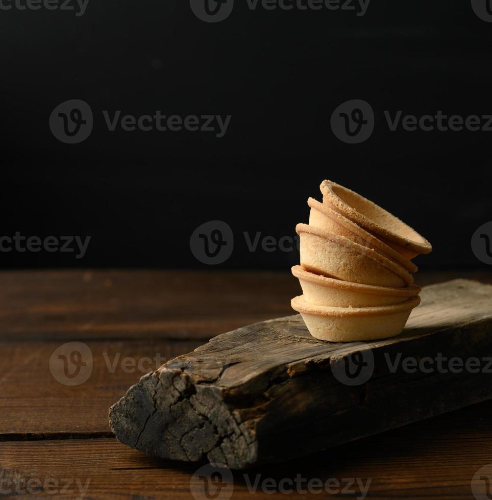 stack av bakad runda tom tartlets på trä- styrelse, svart bakgrund foto