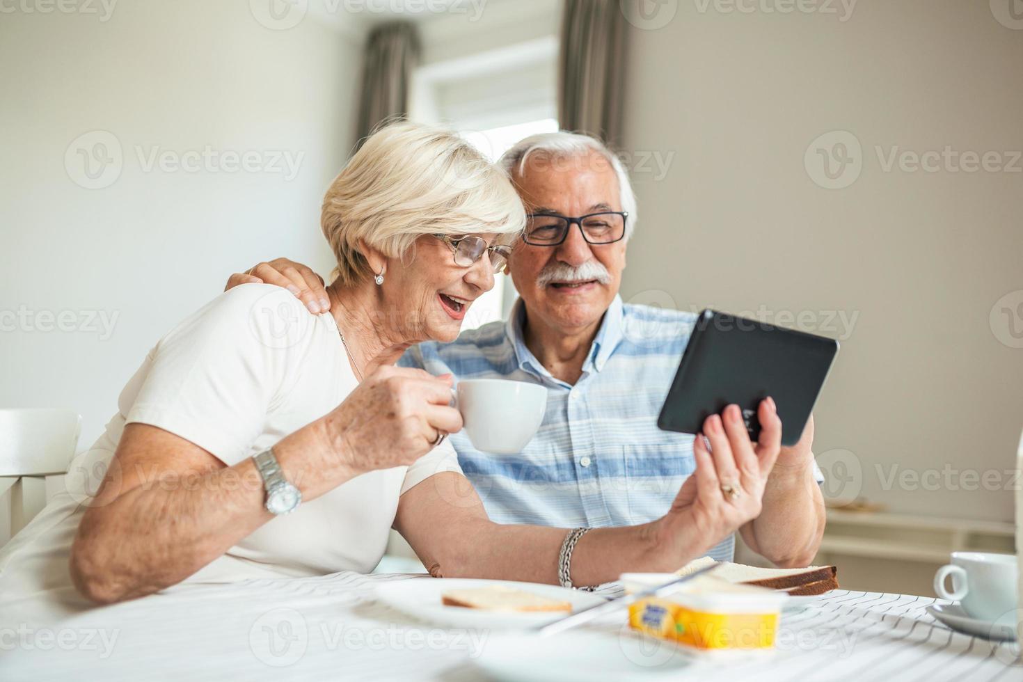 senior man och hans fru är använder sig av en digital läsplatta och kommunicerar med deras ungar. Lycklig senior par är har frukost och har ett uppkopplad konversation med deras familj och sändning hälsningar. foto