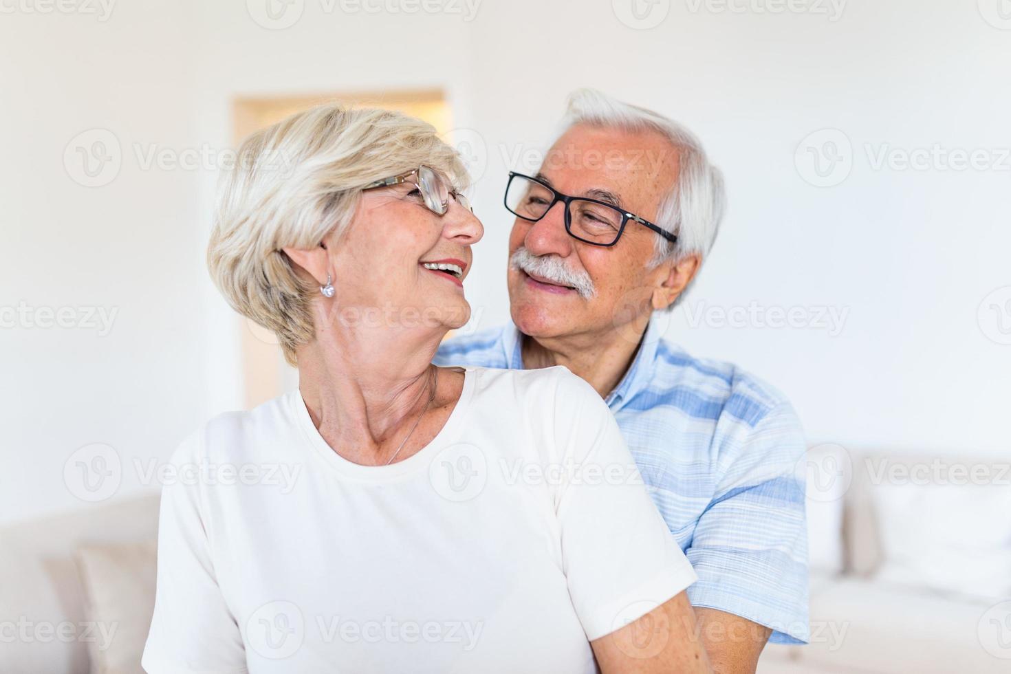 äldre par stående i de levande rum. porträtt av Lycklig senior par fattande varje Övrig i levande rum på Hem. gammal par ser varje Övrig med kärlek och leende. foto