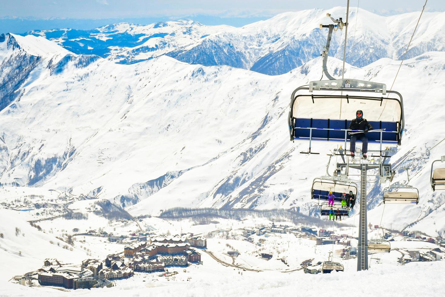 gudauri, georgien, 2022 - skidåkare instruktör sitta på de röding hiss och med ny gudauri åka skidor tillflykt och bergen bakgrund foto