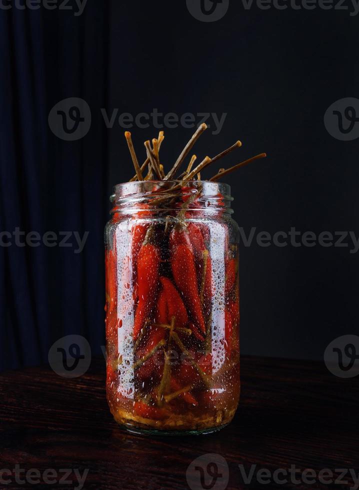 glas burk med inlagd chili paprikor på svart bakgrund foto