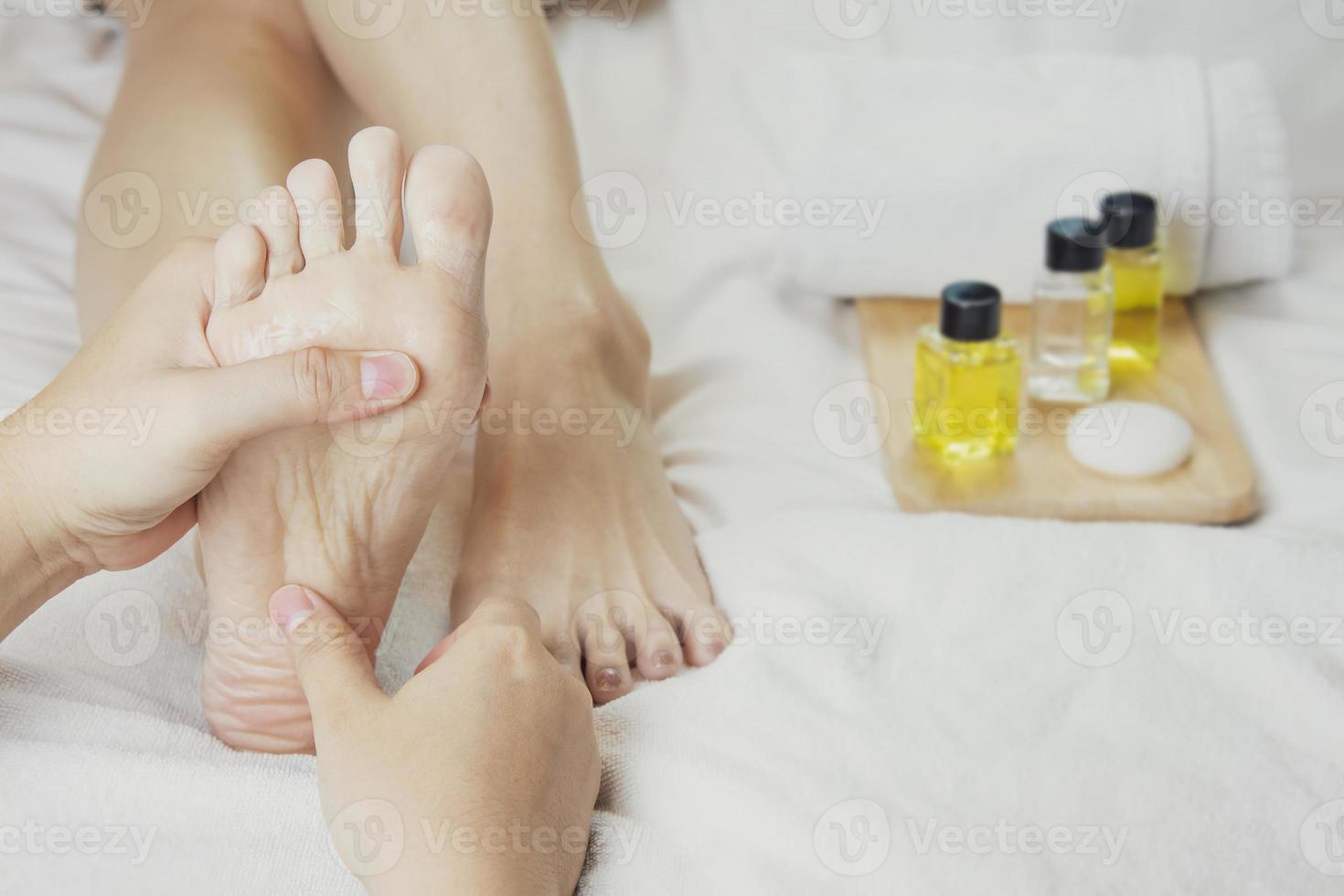 händer av en professionell fot massager med oljor och hälsa vård Produkter på vit säng. begrepp av hälsa vård, avslappning, fot spa behandling. eller produkt introduktion för kvinnors fot spa foto