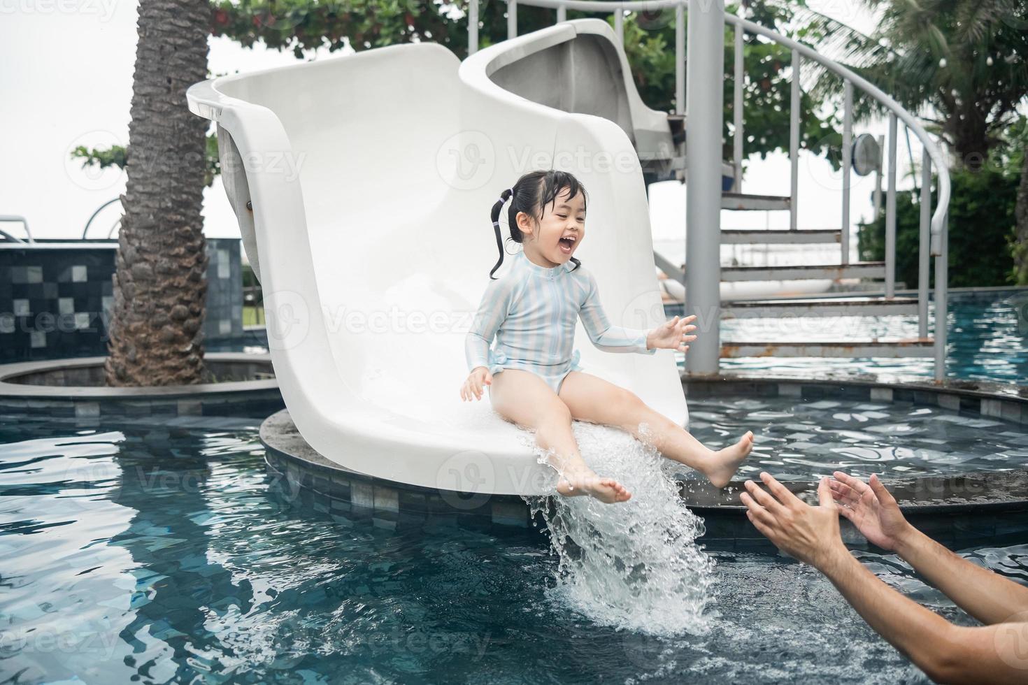 asiatisk far och dotter simning spelar glida slå samman i de slå samman på de tillflykt, leende och skrattande. har roligt i de slå samman på de tillflykt hotell, familj Lycklig begrepp. foto