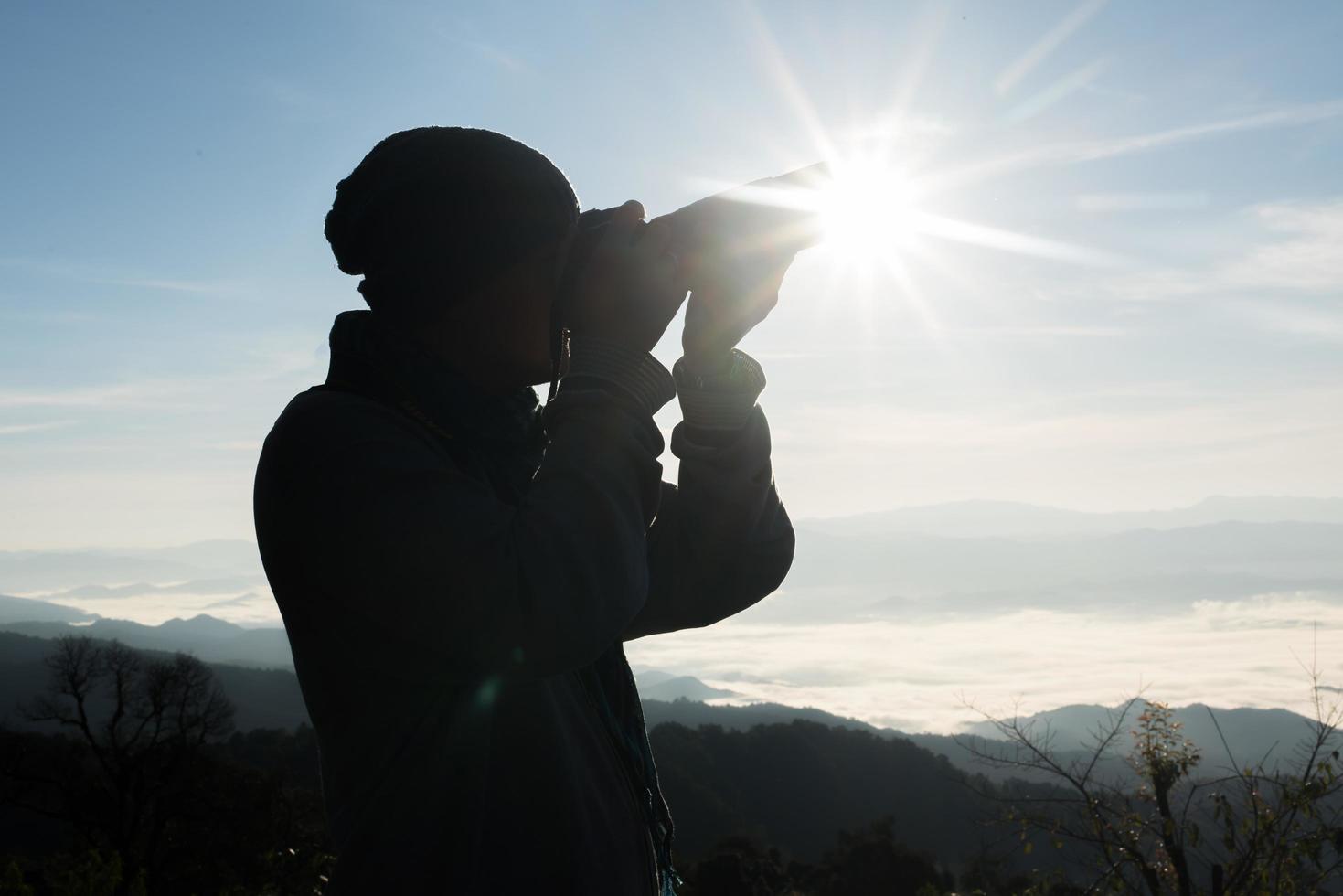 silhuett av ung fotograf som håller en kamera med bergslandskap foto