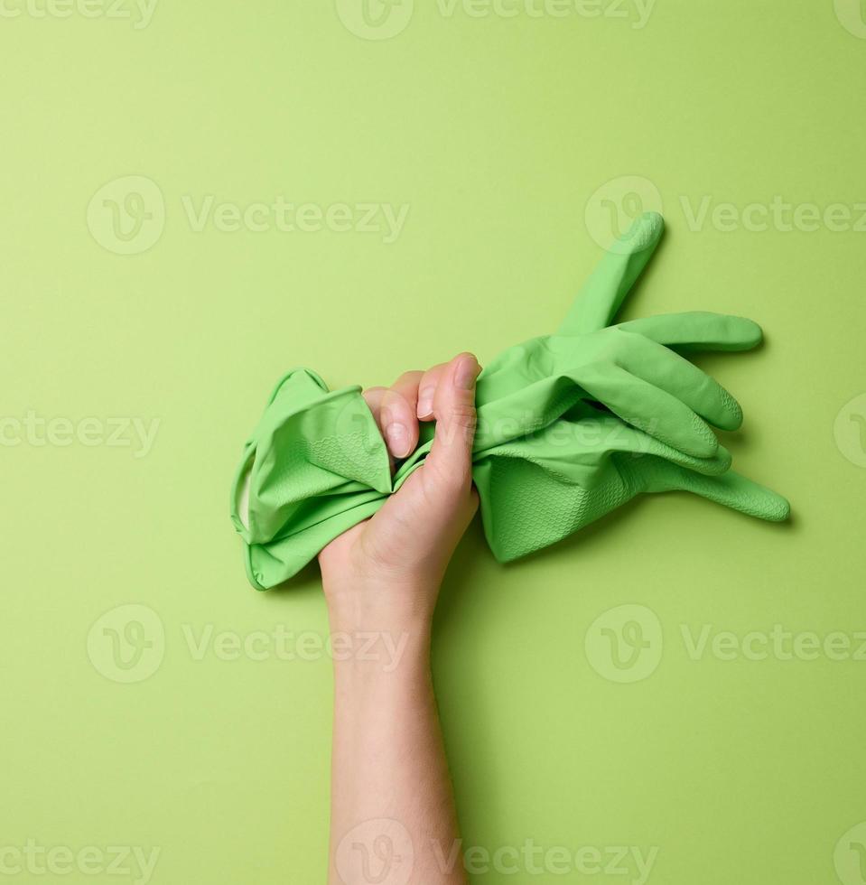 kvinna hand innehar sudd grön handskar för rengöring på en grön bakgrund. del av de kropp är lyft upp foto