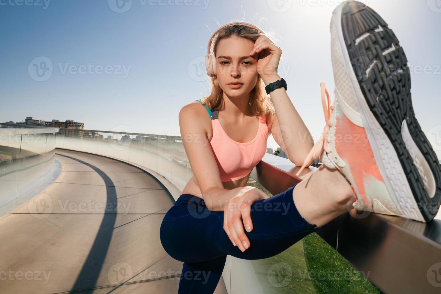 elegant sportigt flicka i hörlurar sträckor de muskler av de ben foto