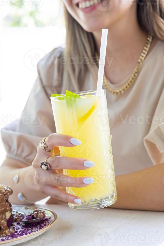 leende kvinna med vit nagel putsa innehav citronsaft. kall citronsaft med citron- och mynta. foto