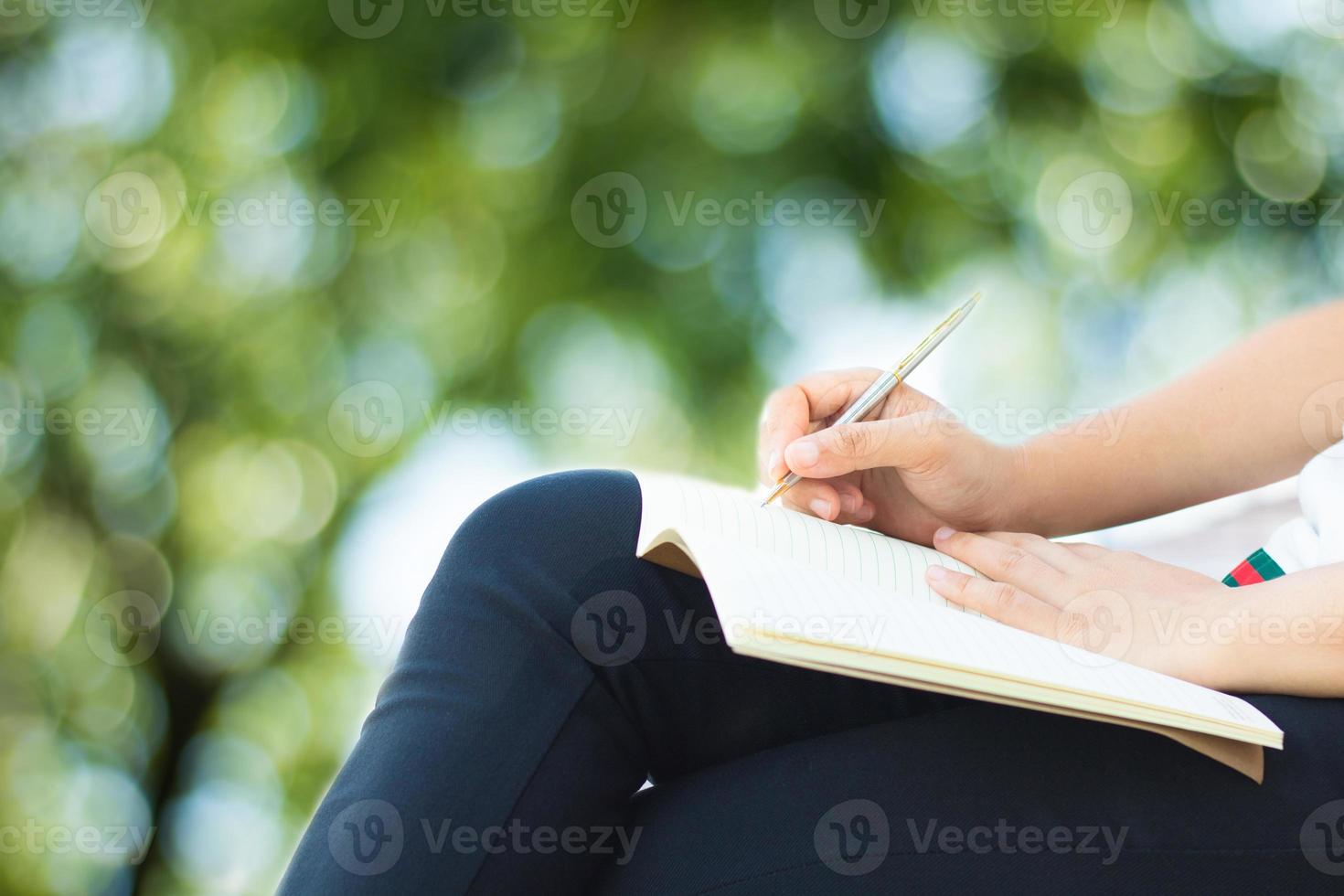 kvinnasammanträde och skriva på anteckningsboken i park foto